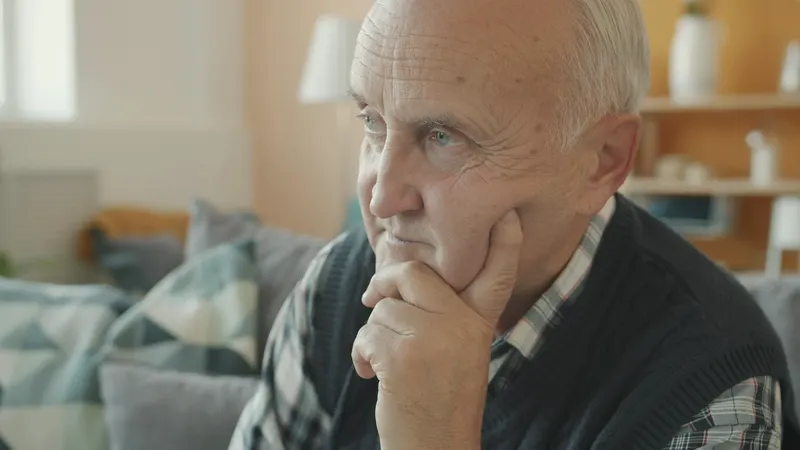 Älterer Mann sitzt nachdenklich im Wohnzimmer